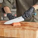 A person in blue gloves using a Schraf Chef Knife with a blue handle to cut salmon on a cutting board.