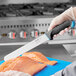 A hand using a Schraf serrated slicing knife to cut a piece of fish.