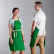 A man and woman wearing Choice kelly green bib aprons with natural webbing accents.