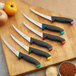 A Schraf boning knife with a black handle in a group of knives on a wooden surface.