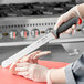 A hand in a glove using a Schraf serrated slicing knife to cut meat on a red counter.