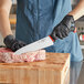 A person in gloves cutting meat on a cutting board with a Schraf chef knife.