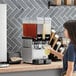 A woman pouring liquid into a Vollrath refrigerated beverage dispenser.