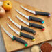 A Schraf yellow boning knife with black and red knives on a cutting board.