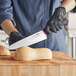 A person in black gloves using a Schraf chef knife to cut on a wooden cutting board.