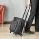 A man using a ServIt Trolley Cooler Bag with a telescoping handle and wheels.