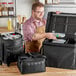 A man in an apron opening a black ServIt delivery bag with a strap.