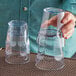 A woman's hand holding two Choice clear plastic paneled tumblers filled with liquid.