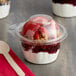 A Dart plastic container of yogurt with strawberries and granola with a dome lid.