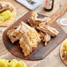 A wooden cutting board with a pile of cooked ribs and corn on the cob on it.