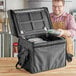 A man in an apron putting food containers in a black ServIt delivery bag.