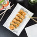 A rectangular white porcelain platter with a bamboo pattern holding sushi with chopsticks.