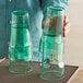 A man holding two green Choice plastic paneled tumblers full of green liquid.