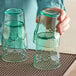 A hand holding two green Choice plastic tumblers on a table.