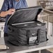 A man in a chef's uniform opening a large black Vollrath food pan carrier bag.