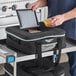 A man putting food containers into a black and grey Vollrath insulated snack delivery bag.