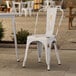 A white Lancaster Table & Seating outdoor cafe chair on a patio.