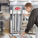 A man in a black shirt using an Avantco stainless steel manual sausage stuffer in a kitchen.