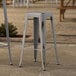 Lancaster Table & Seating Distressed Nickel Gray Outdoor Backless Barstools sitting on a stone surface.