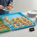 A person serving food on a blue bakery tray on a table with other trays.