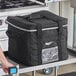 A man using a Vollrath insulated black bag to hold a milk crate on a table.