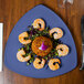 A GET Diamond Mardi Gras peacock blue melamine triangle plate with shrimp and a salad on it.