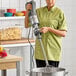 A woman in a green shirt using a Robot Coupe immersion blender with a whisk attachment in a professional kitchen.