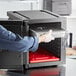 A person opening a CaterGator Dash black metal container in a school kitchen.