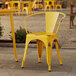 A Lancaster Table & Seating distressed citrine yellow outdoor arm chair on a stone patio next to a table.