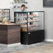 A woman behind a Avantco dry bakery display case with pastries.