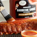 A hand using a paint brush to add Sauce Craft Original BBQ Sauce to a piece of meat.