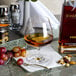 A Stolzle brandy snifter filled with brown liquid next to a bottle of liquor and grapes.