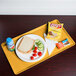 A Cambro mustard dietary tray with a sandwich, chips, and a drink on it.