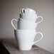 A stack of Tuxton white Europa China cappuccino mugs.