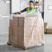 A man in a safety vest and gloves pushing a Lavex clear plastic pallet cover over a pallet of boxes.
