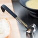 A Vollrath Jacob's Pride stainless steel ladle with a short black handle sitting next to a bowl of soup.
