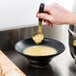 A person using a Vollrath Jacob's Pride stainless steel ladle with a short black handle to spoon soup into a bowl.