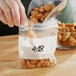 A person wearing gloves pouring nuts into a Choice 4" x 4" clear plastic bag.