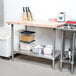 An Advance Tabco wood top work table with a stainless steel base and undershelf in a professional kitchen.