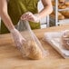 A woman in a green apron using a Choice bread bag to package a loaf of bread.