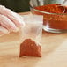 A gloved hand holding a clear LDPE zip top bag of red chili powder.