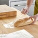 A person in a green apron using a wicket dispenser to put a clear plastic bag on a loaf of bread.