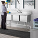 A woman in blue gloves washing a Regency stainless steel 3 compartment sink with a left drainboard.