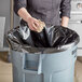A person throwing a crumpled paper into a black heavy-duty trash bag.