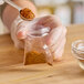 A hand holding a Choice 2" x 2" clear LDPE zip top bag of spices with a spoon.