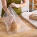 A woman in a green apron putting a loaf of bread in a Choice clear plastic bread bag.