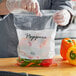 A person in gloves holding a Choice clear polyethylene zip top bag of peppers.