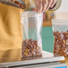 A close-up of a person's hand putting nuts into a Choice clear zip top bag on a counter.
