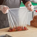 A person in a chef's uniform holding a Choice clear polyethylene layflat bag of food.