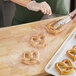 A person using tweezers to put a salted pretzel in a clear plastic bag.